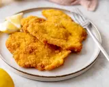 Piatto di cotolette di pollo dorate e croccanti, servite con spicchi di limone fresco e una forchetta.