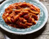 Un piatto fumante di trippa alla romana, ricca di sugo di pomodoro e condita con pecorino grattugiato, servita su un piatto decorato.