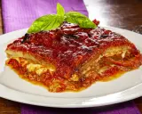 Una fetta di parmigiana di melanzane al forno, ricca e succulenta, guarnita con basilico fresco.