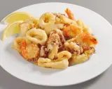 Un invitante piatto di frittura di pesce, con anelli di calamari dorati e gamberi croccanti, guarnito con spicchi di limone fresco.