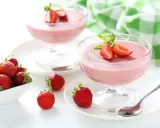 Deliziosa mousse di fragole in coppette di vetro, guarnita con fragole fresche e menta. Accanto, fragole in una ciotola bianca.