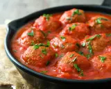 Polpette di carne succulente in salsa di pomodoro, guarnite con prezzemolo fresco, servite in una padella di ghisa.