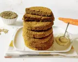 Impilati hamburger di lenticchie dorati, con lenticchie secche, carote e una salsa cremosa in un piatto.