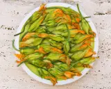 Fiori di zucca freschi, pronti per essere cucinati in padella, su un piatto bianco.