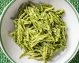 Un piatto di trofie al pesto, pasta fresca condita con un sugo verde brillante, servita in una ciotola bianca su una tovaglietta colorata.