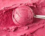 Un cucchiaio raccoglie una porzione di cremoso gelato fatto in casa, dal colore rosa intenso, su uno sfondo dello stesso dolce freddo.