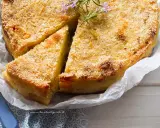 Delizioso gateau di patate dorato e croccante, guarnito con rosmarino fresco. Una fetta è già stata tagliata, invitando ad assaporare questo piatto saporito.
