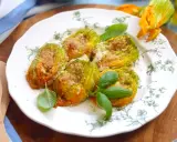 Deliziosi fiori di zucca al forno, ripieni e dorati, guarniti con basilico fresco su un piatto decorato.