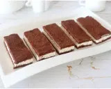 Sei fette di torta kinder fetta al latte, con pan di spagna al cacao e crema bianca, disposte su un piatto bianco.