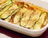 Sformato di zucchine appena sfornato, con fette sottili di zucchina grigliata, prosciutto e formaggio filante, condito con pepe nero.