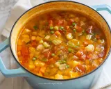 Un fumante minestrone di verdure in una pentola azzurra, ricco di carote, zucchine, piselli e pomodoro.