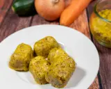 Cinque cubetti dorati di dado vegetale fatto in casa, preparati con carote, zucchine e cipolle, su un piatto bianco.