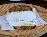 Ricotta al forno dorata e profumata con erbe aromatiche, servita su un tagliere di legno.
