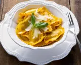 Un piatto invitante di tortelli di zucca, guarniti con scaglie di parmigiano e una fogliolina di basilico, pronti per essere gustati.
