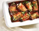 Involtini di melanzane ripieni di formaggio, cotti in sugo di pomodoro e guarniti con prezzemolo fresco.