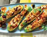 Zucchine ripiene vegetariane con pinoli, olive e erbe aromatiche, servite su un piatto azzurro con un filo d'olio piccante.