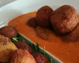 Polpette di pane dorate e croccanti, servite su una salsa rossa cremosa e guarnite con rucola fresca.