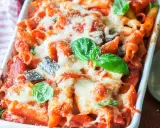 Piatto fumante di pasta al forno con melanzane, ricoperta di formaggio fuso e basilico fresco.