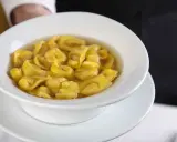 Un piatto fumante di tortellini in brodo, un classico comfort food italiano, servito in una ciotola bianca.