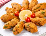 Deliziose polpette di lenticchie, disposte a cerchio su un piatto bianco, con spicchi di limone e pomodorini ciliegino.