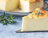Una fetta di torta di ricotta soffice e dorata, guarnita con rosmarino, su un piatto da torta argentato.