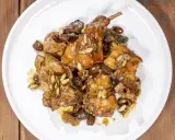 Pezzi di coniglio alla ligure, cotti con olive, pinoli e erbe aromatiche, serviti su un piatto bianco.