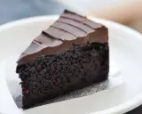 Una fetta di torta al cioccolato senza burro, soffice e ricoperta da glassa al cioccolato, servita su un piatto bianco.