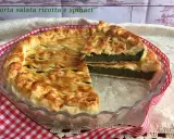 Torta salata ricotta e spinaci dorata e invitante, con una fetta tagliata che mostra il ripieno verde e cremoso.