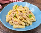 Piatto di pasta tonno e limone, condita con tonno sfilacciato, scorza di limone e basilico fresco, servita in un piatto blu.
