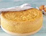 Un soffice pan di spagna dorato, coperto da un canovaccio, con uova fresche sullo sfondo.