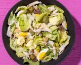 Insalata di pollo ricca con lattuga, uova sode, olive verdi e acciughe, condita con maionese.