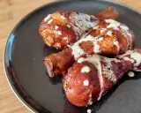 Tre succulenti fusi di pollo arrostiti, conditi con spezie e nappati con una cremosa salsa bianca, serviti su un piatto scuro.