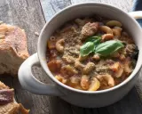 Una ciotola di pasta e fagioli in scatola, guarnita con basilico fresco e pane croccante su un tavolo di legno.