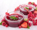 Due coppette di coulis di lamponi, guarnite con lamponi freschi, ribes e foglie di menta, circondate da fragole e frutti di bosco.