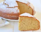 Una fetta di torta di banane soffice, cosparsa di zucchero a velo, accanto alla torta intera su un piatto bianco.