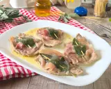 Saltimbocca alla romana: fettine di vitello con prosciutto e salvia, servite su un piatto bianco con salsa dorata.