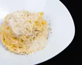 Un piatto di spaghetti cacio e pepe, cremosi e ricchi, cosparsi di pepe nero macinato fresco e formaggio grattugiato.