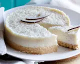 Delizioso cheesecake al cocco, ricoperto di cocco grattugiato e decorato con scaglie di cocco fresco. Una fetta è già stata tagliata.