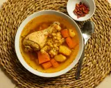 Un confortante brodo di pollo con pezzi di pollo, carote e patate, servito su una tovaglietta di paglia.