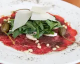 Delicato carpaccio di manzo con rucola, scaglie di parmigiano, pinoli, capperi e funghi champignon.