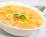Una ciotola di zuppa cremosa con pezzi di patate e riso, guarnita con una foglia verde. Un piatto confortante che sa di casa.