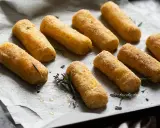 Crocchette di patate al forno dorate e croccanti, adagiate su carta forno con rametti di rosmarino e fiori di lavanda.