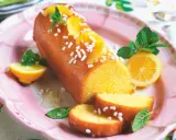 Deliziosa torta al limone glassata, decorata con fette d'arancia, zuccherini e menta. Servita su un piatto rosa con spicchi di limone.