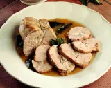 Delizioso arrosto di tacchino affettato, servito con salsa e foglie di salvia su un piatto bianco.