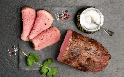 Una succulenta lombata di vitello, affettata e pronta per essere gustata, accompagnata da sale grosso, pepe e un rametto di coriandolo.