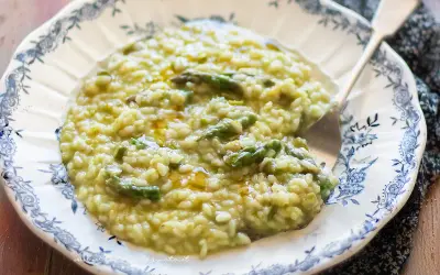Un cremoso risotto con asparagi, servito in un piatto decorato con un motivo blu. Un piatto primaverile invitante.