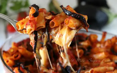 Un primo piatto fumante di pasta alla norma, con melanzane fritte, pomodoro e tanto formaggio filante che si allunga.