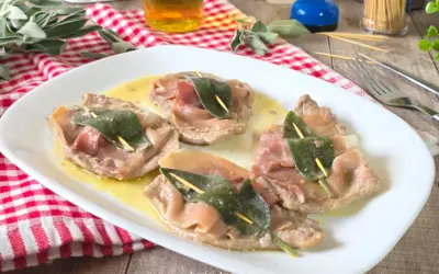 Saltimbocca alla romana: fettine di vitello con prosciutto e salvia, servite su un piatto bianco con salsa dorata.