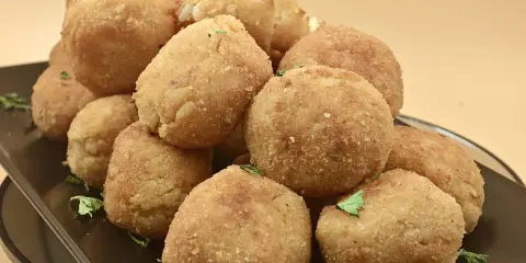 Un mucchio invitante di polpette di riso dorate e croccanti, guarnite con prezzemolo fresco, su un piatto scuro.