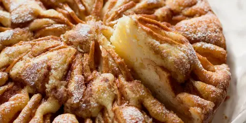 Una deliziosa torta di mele, cosparsa di zucchero a velo, con una fetta appena tolta che rivela la morbidezza dell'interno.